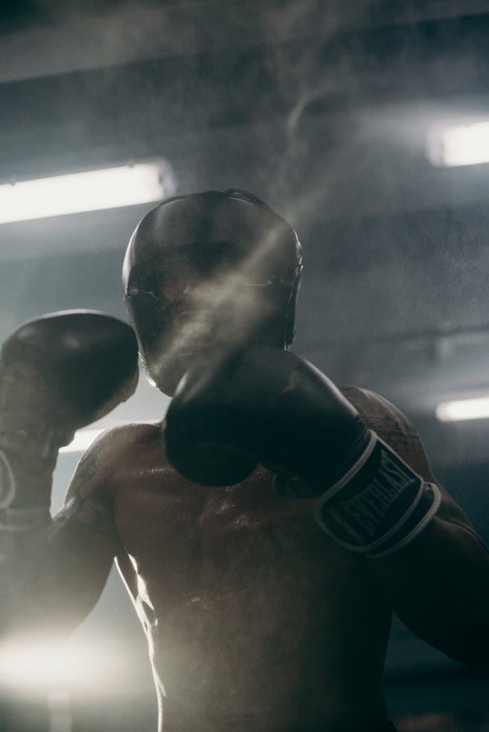 A focused boxer practices his punches in a shadowy gym, creating an intense atmosphere.